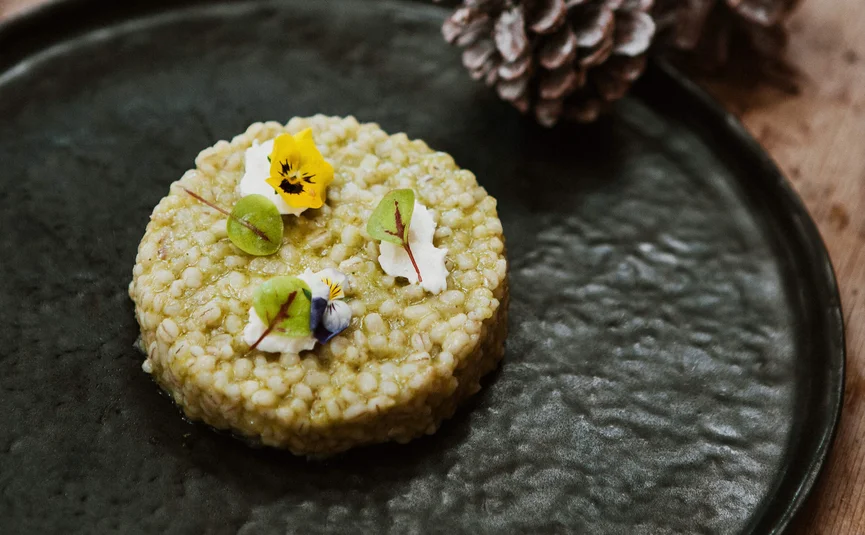 Kreisförmiges Gericht aus Gerste mit essbaren Blüten auf schwarzem Teller