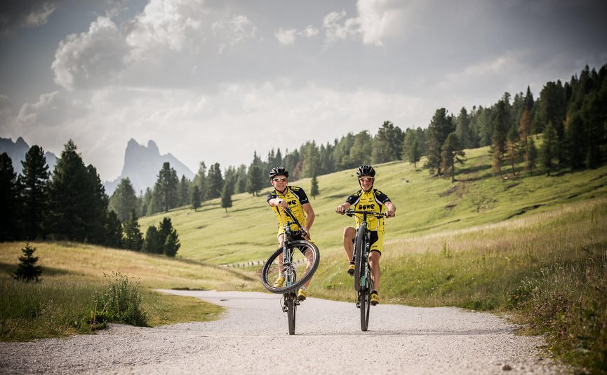 Zwei Radfahrer machen Wheelies auf einem Feldweg in den Bergen
