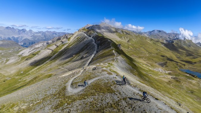 Mountainbiker auf einem Höhenweg in alpiner Landschaft bei klarem Himmel