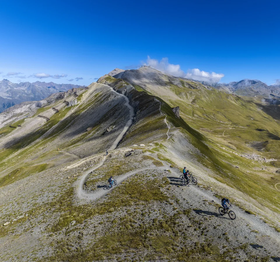 Mountainbiker auf einem Höhenweg in alpiner Landschaft bei klarem Himmel