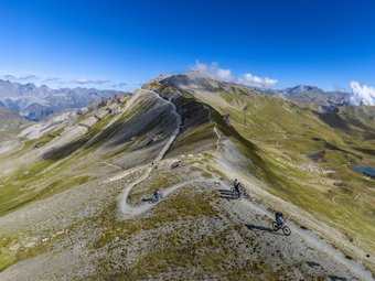 Mountain bikers riding on a ridge trail in alpine mountain landscape under blue sky