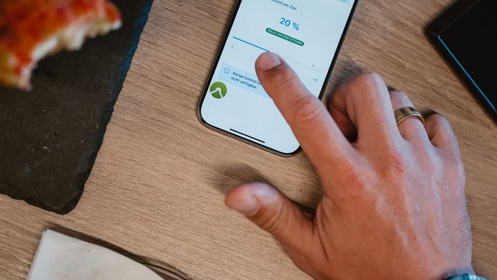 Das Abenteuer ruft und dein eBike hört zu! © Bosch eBike Systeme Hand bedient Smartphone mit Range Control App neben Croissant und Pizza