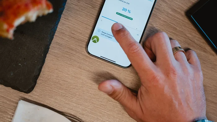 Das Abenteuer ruft und dein eBike hört zu! © Bosch eBike Systeme Hand bedient Smartphone mit Range Control App neben Croissant und Pizza