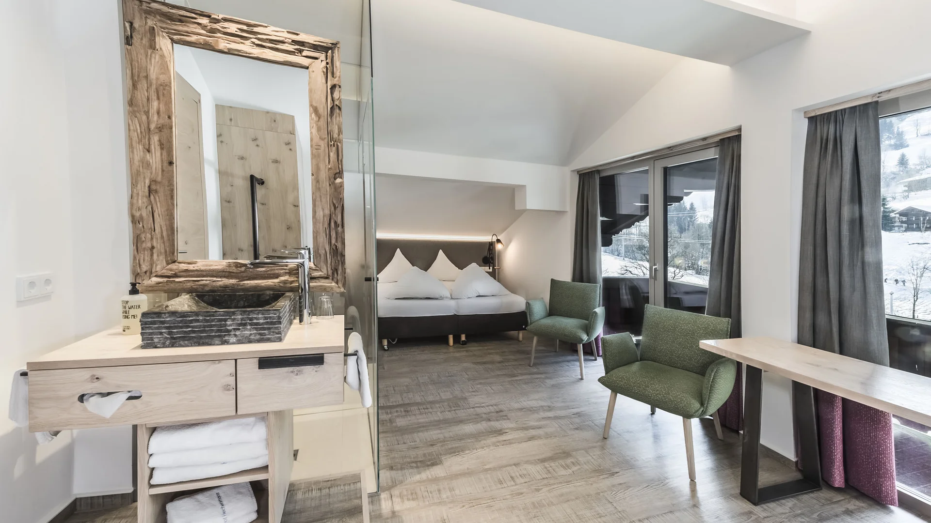 Modernes Hotelzimmer mit Bett, Waschbecken und Sitzbereich mit Bergblick