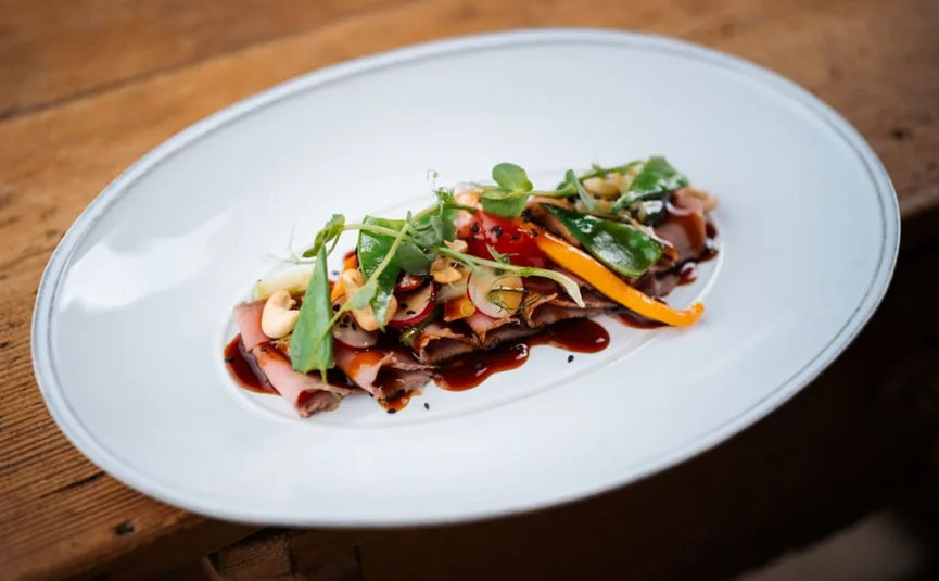 Plated thinly sliced meat with vegetables and sauce on a white dish