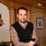 Mann sitzt auf Weinfass mit Weinflaschen und Glas in gemütlichem Raum