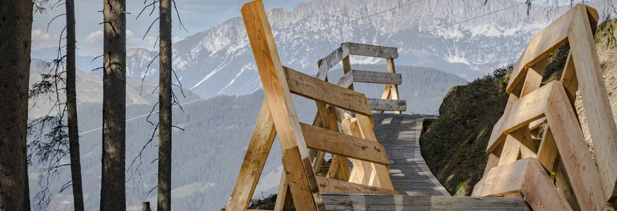 Neuer Flow im Brixental: Der Kirchberg Trail eröffnet © Stromberg Holzsteg mit Geländer im Bergwald mit Aussicht auf Berge