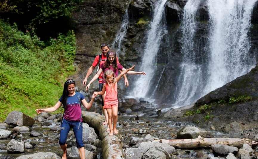 Family barefoot hiking crossing log near waterfall