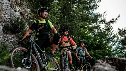 Three mountain bikers with helmets resting on rocky trail in forest