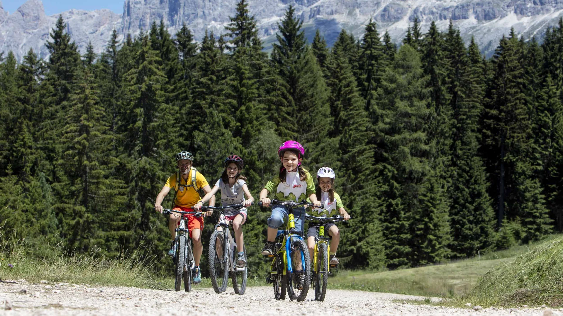 Familie fährt Mountainbikes auf Waldweg vor Bergkulisse