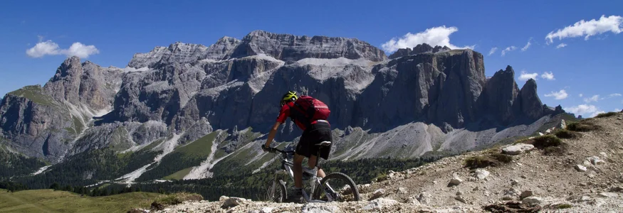 Mountainbiker fährt auf felsigem Pfad mit Bergen und blauem Himmel im Hintergrund