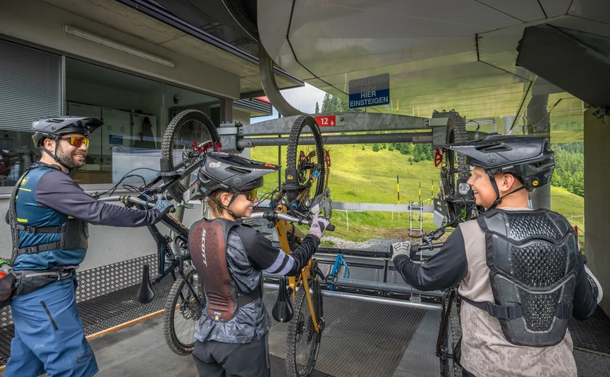 Drei Fahrradfahrer mit Helmen laden Bikes in eine Seilbahn an einem Berg