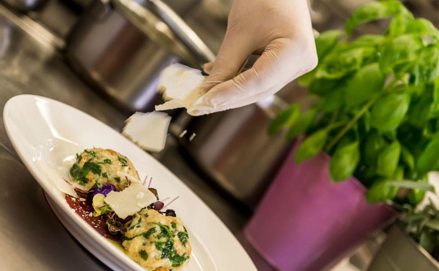 BIKE BREAK (7 Nächte) Hand mit Handschuhen bestreut Käse über ein Gericht mit Kräutern