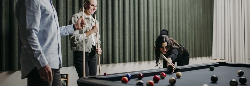 Drei Personen spielen gemeinsam Billard in einem modernen Raum