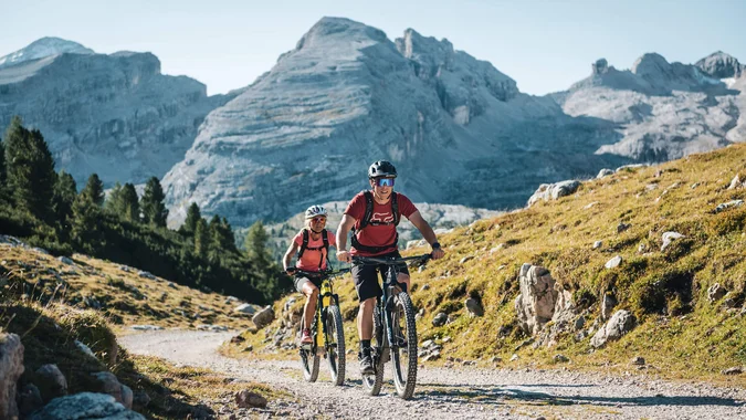 Zwei Mountainbiker fahren auf einem Bergweg vor großen Bergen