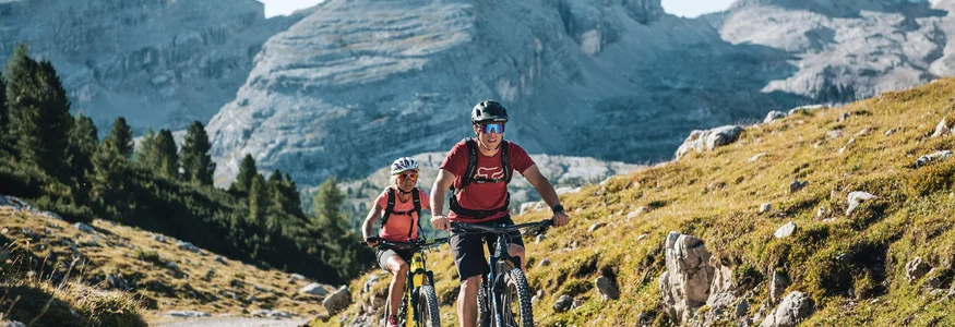 Mountainbike-Saisonstart am Kronplatz © Alex Moling Zwei Mountainbiker fahren auf einem Bergweg vor großen Bergen