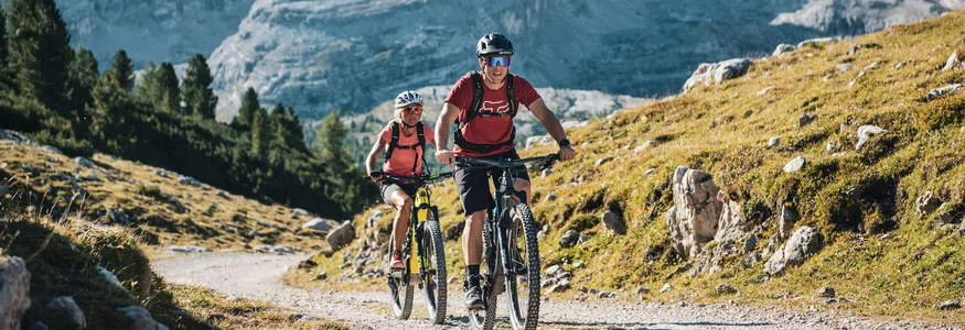 Zwei Mountainbiker fahren auf einem Bergweg vor großen Bergen