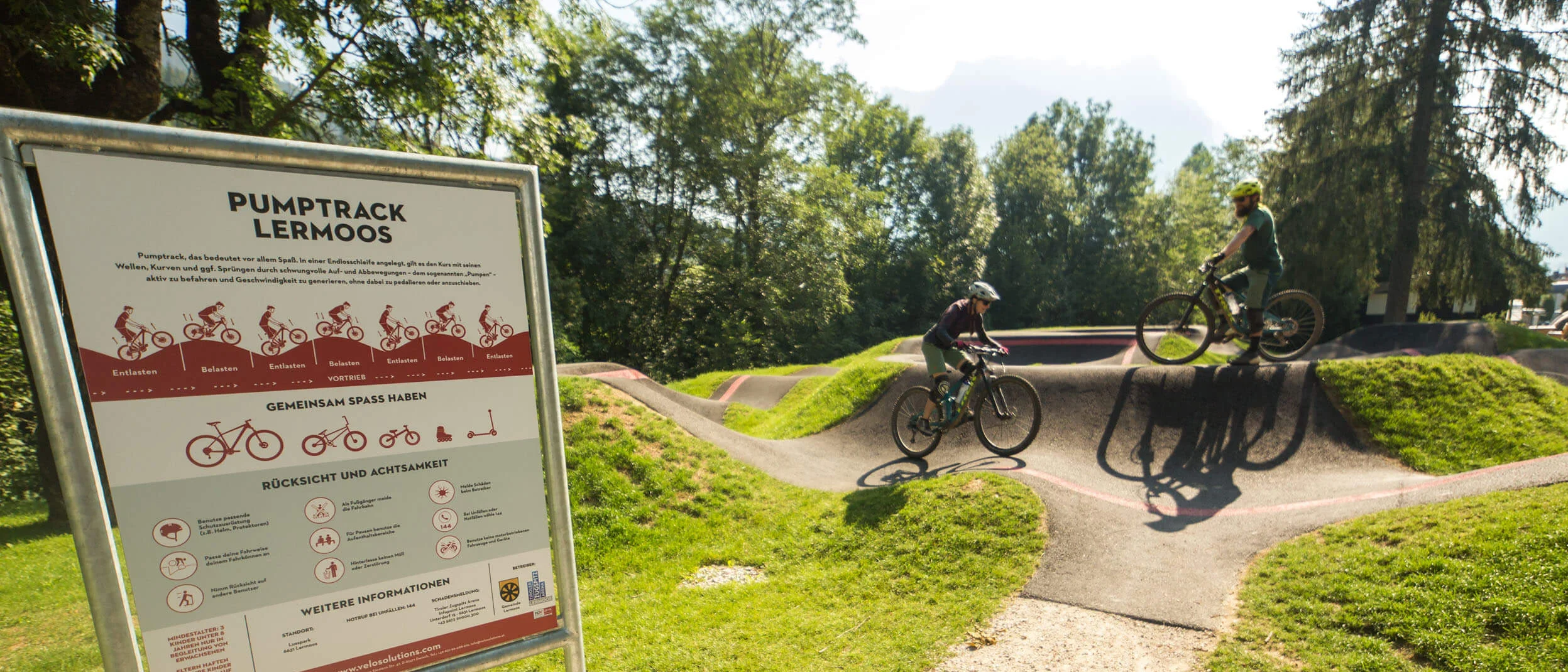 Pumptrack in Lermoos mit zwei Radfahrern und einem Info-Schild