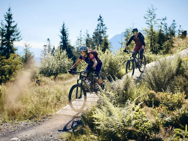 Unterwegs in Österreichs größter Bikeregion © Tobias Köhler Zwei Mountainbiker fahren einen Trail in bewaldeter Berglandschaft