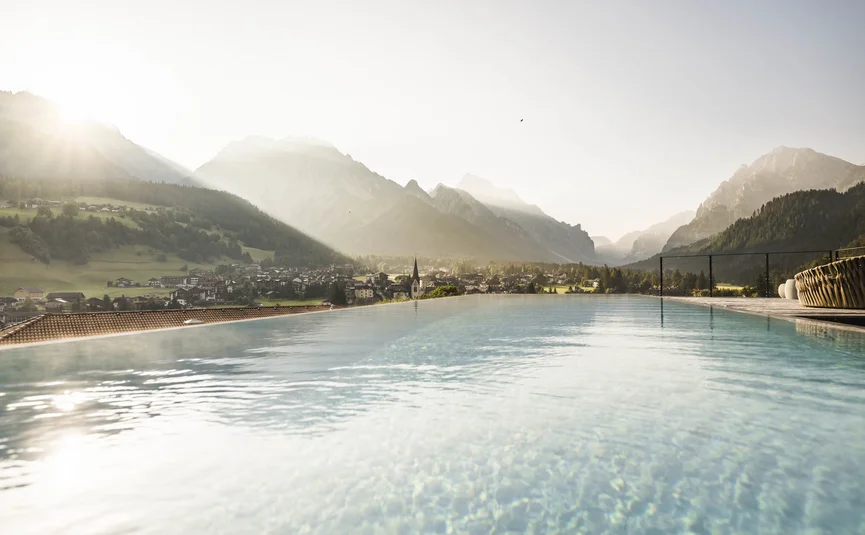 Mountain village with sun rays over the infinity pool in the morning