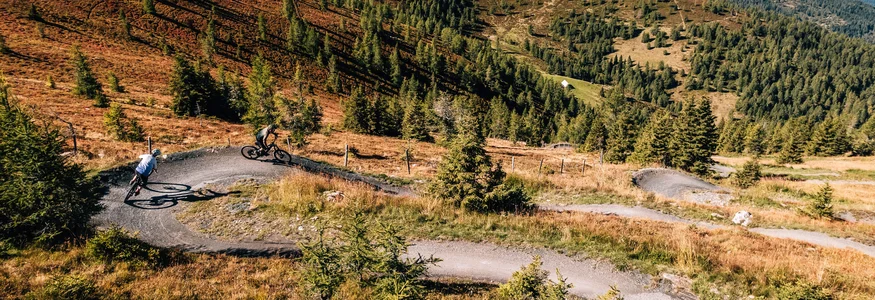 Twee mountainbikers op een kronkelig bospad in de bergen bij helder weer