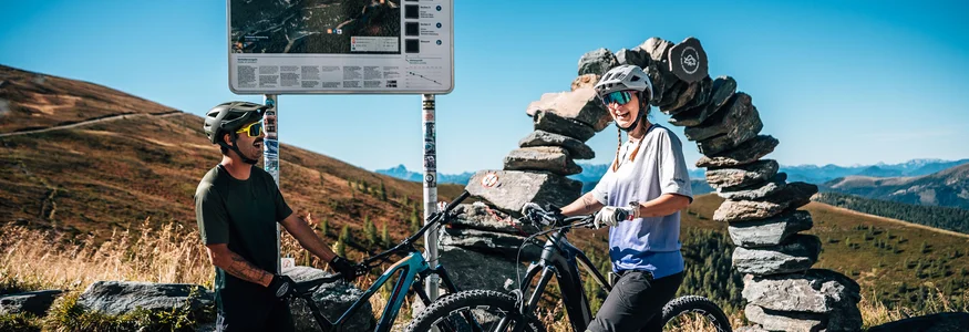 Twee mountainbikers met fietsen bij een routebord in de bergen