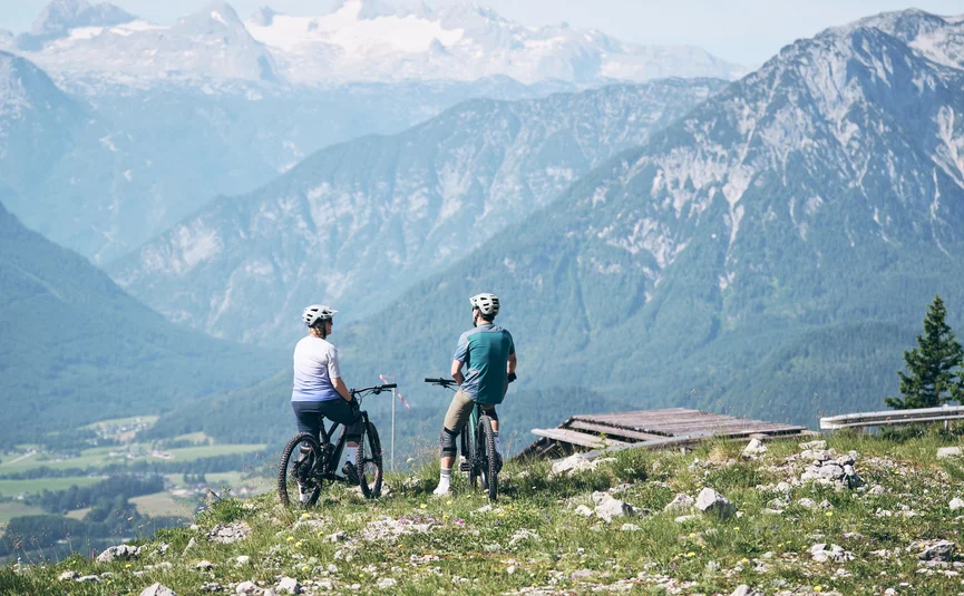 Two cyclists standing on grassy hill overlooking mountains