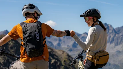 Zwei Mountainbiker mit Helm geben sich auf Berglandschaft die Faust
