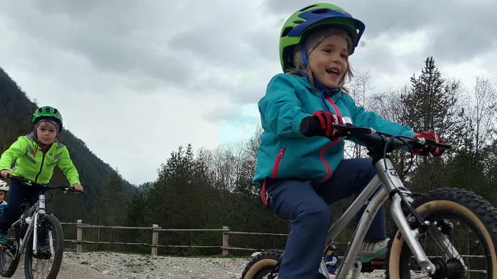 Drei Kinder fahren Mountainbikes auf einer kiesigen Strecke bei bewölktem Himmel