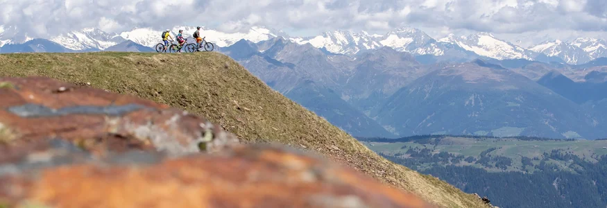 Drei Radfahrer auf einem Berg mit schneebedeckten Alpen im Hintergrund