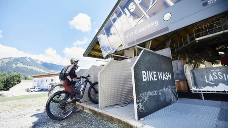 Fahrradwaschanlage im Freien mit zwei Radfahrern und Bergkulisse