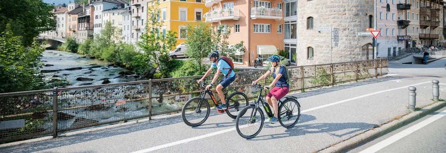 Zwei Radfahrer fahren an einem Fluss und historischen Gebäuden entlang