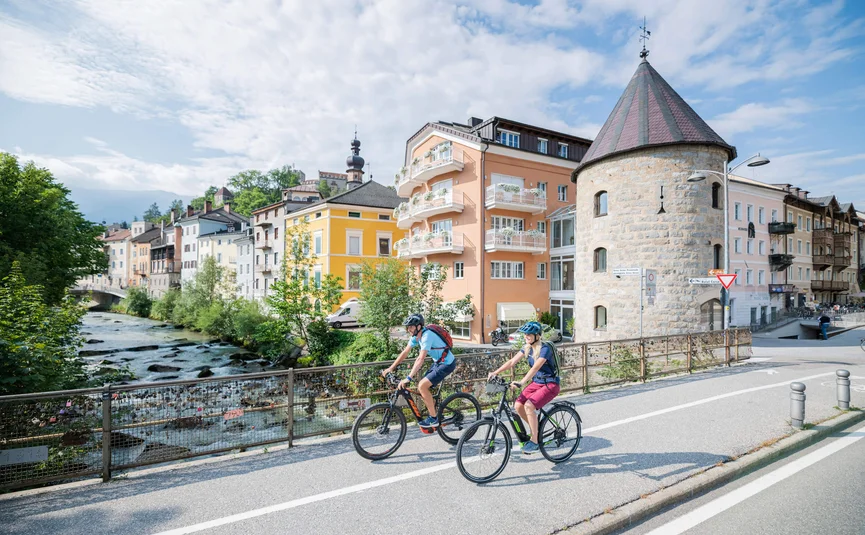 Zwei Radfahrer fahren an einem Fluss und historischen Gebäuden entlang