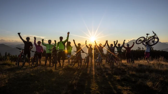Groep fietsers steekt handen op bij zonsondergang in de bergen