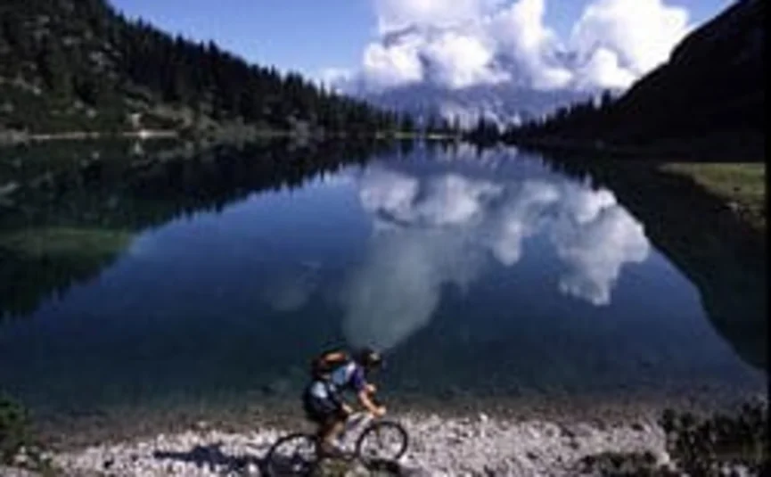 Cyclist by the shore of a mountain lake with cloud reflections