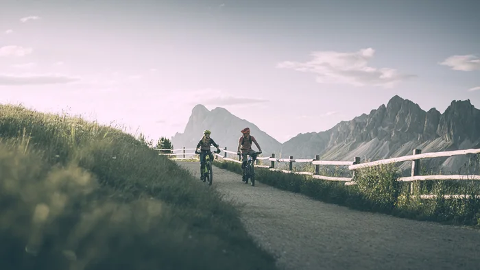Zwei Radfahrer auf einem Bergweg mit Bergen im Hintergrund