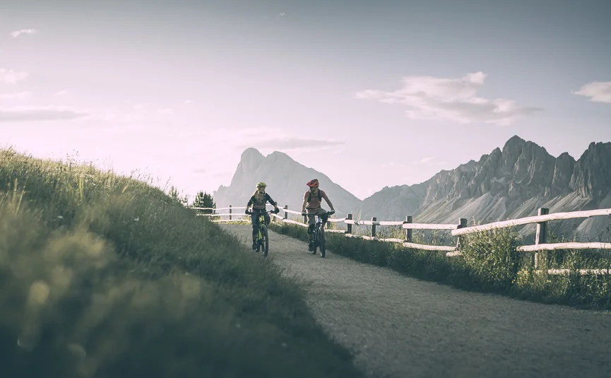 Zwei Radfahrer auf einem Bergweg mit Bergen im Hintergrund