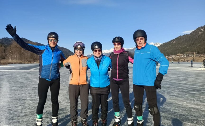 Vijf mensen poseren op schaatsen op bevroren meer met bergen op de achtergrond