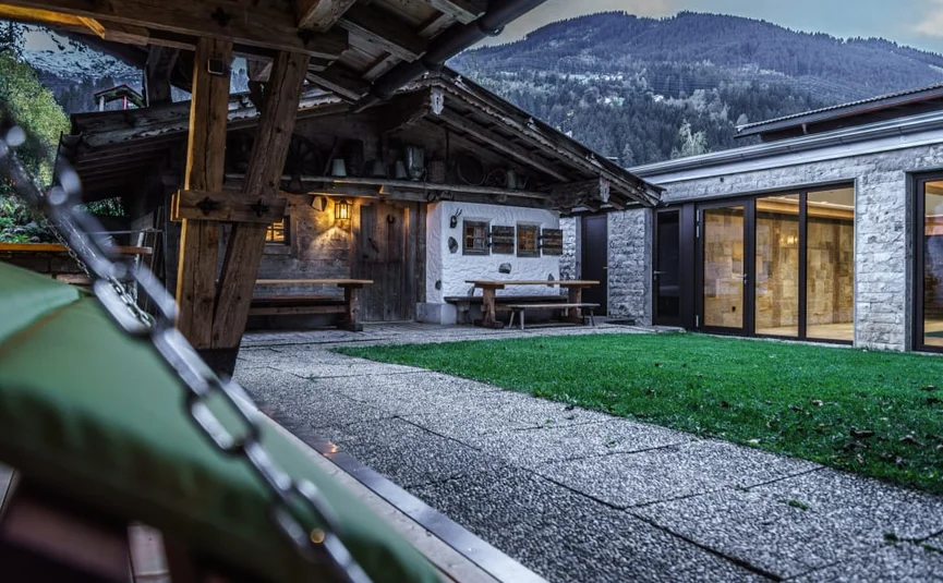 Innenhof mit altem Holzhaus und modernem Gebäude vor Bergkulisse