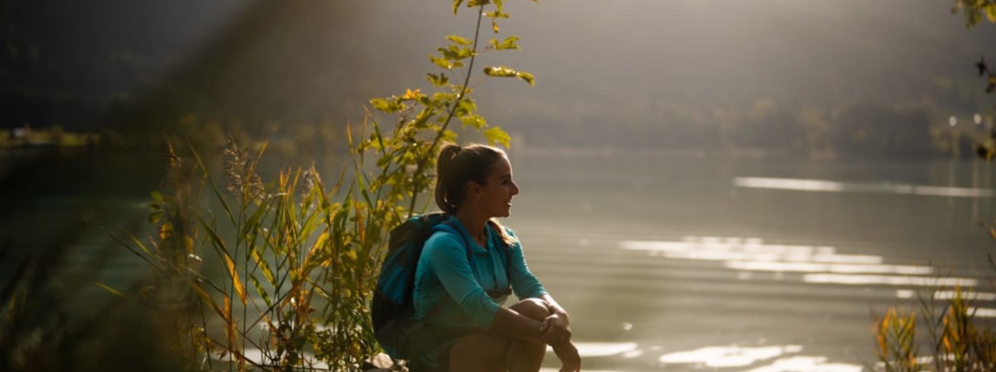 Vrouw met rugzak zittend aan meer genietend van berglandschap