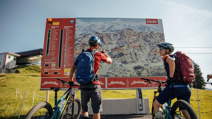 Zwei Mountainbiker sehen auf eine große KitzSki-Karte mit Routen und Lifts.