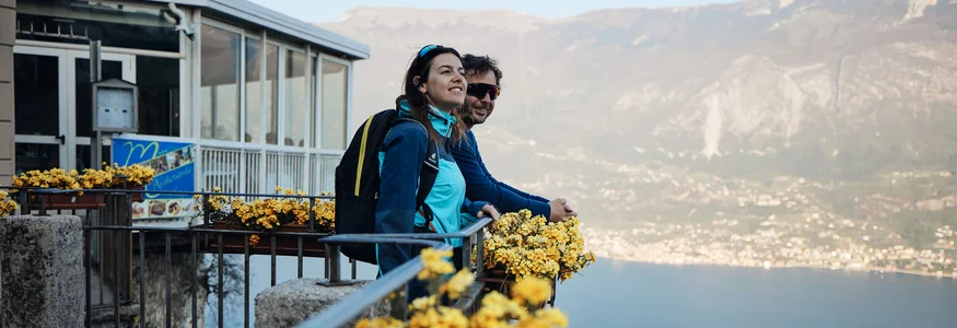 Unterwegs auf der Bond-Straße © Tobias Köhler Zwei Wanderer genießen die Aussicht über den See von einem Balkon mit gelben Blumen