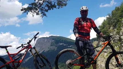 Mountainbiker met twee fietsen op rotsachtig bergpad met klif en lucht