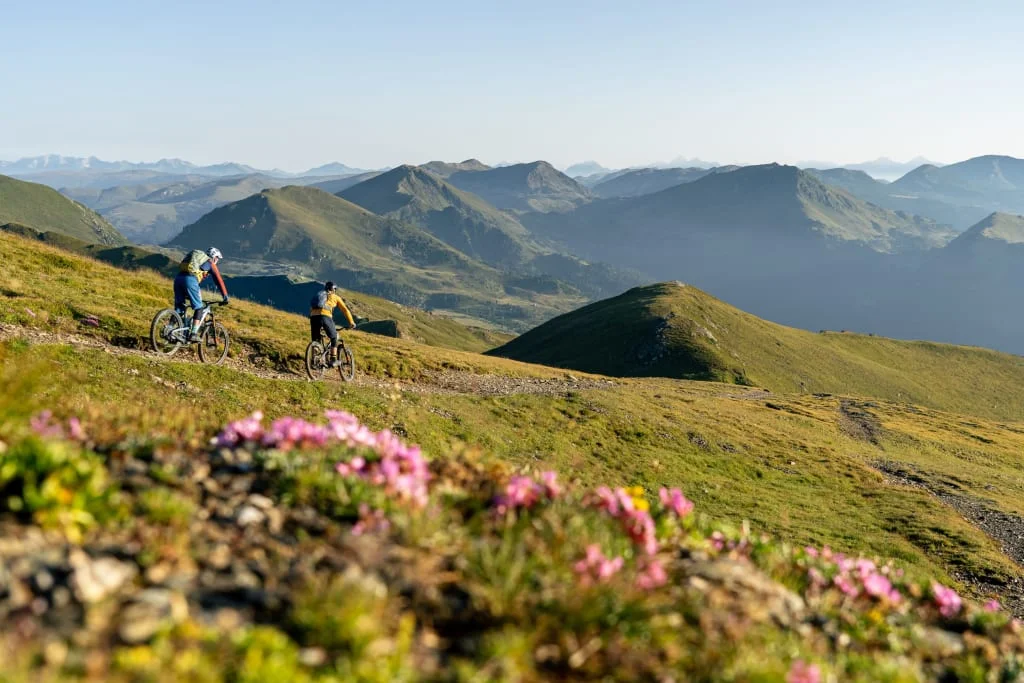 Two mountain bikers riding on a trail with alpine mountain views