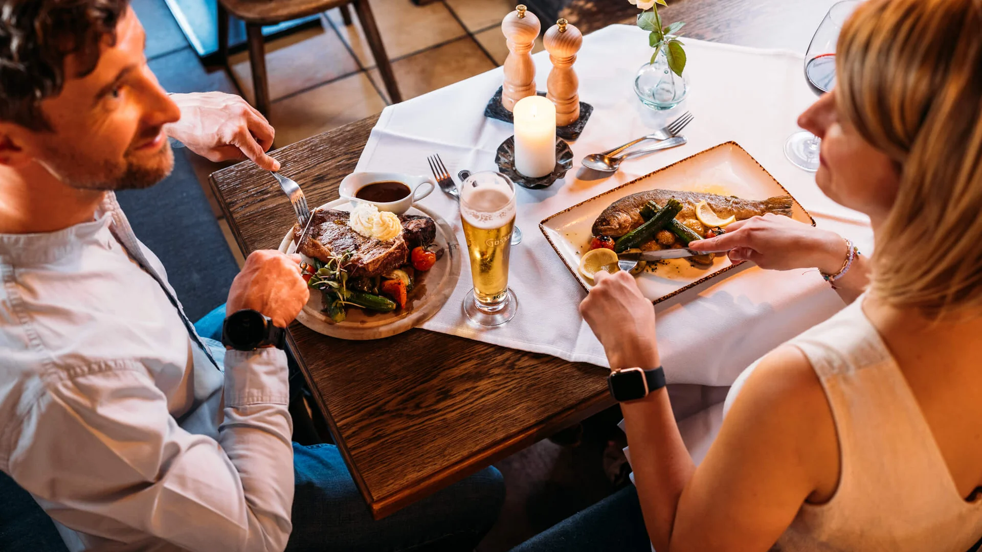 Paar beim Essen in Restaurant mit Steak und Fisch an einem gedeckten Tisch