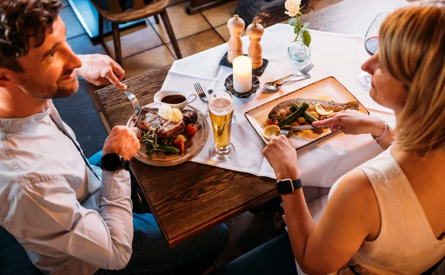Paar beim Essen in Restaurant mit Steak und Fisch an einem gedeckten Tisch