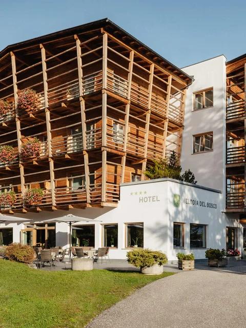 Hotel Melodia del Bosco mit Holzfassade und Blumen auf Balkonen im Grünen