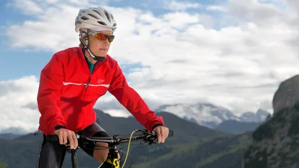 Frau mit roter Jacke und Helm fährt Mountainbike in den Bergen