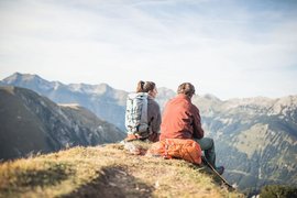 Twee wandelaars zitten op een berg met rugzakken uitkijkend over bergen