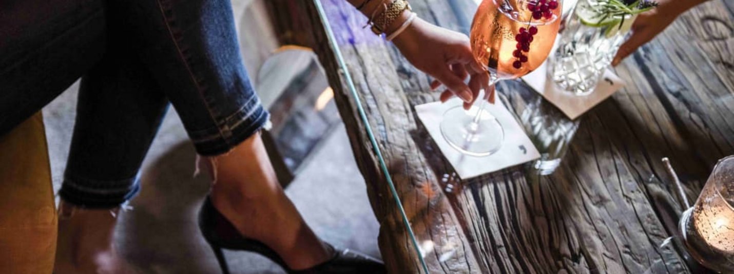 LADY DAYS Woman in high heels reaching for a drink on a rustic wooden table